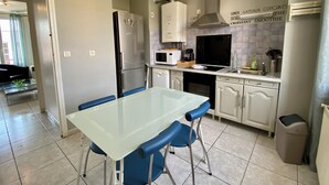 Una cocina moderna con una mesa de comedor de vidrio, sillas azules, un refrigerador de acero inoxidable, un microondas y una estufa a gas.