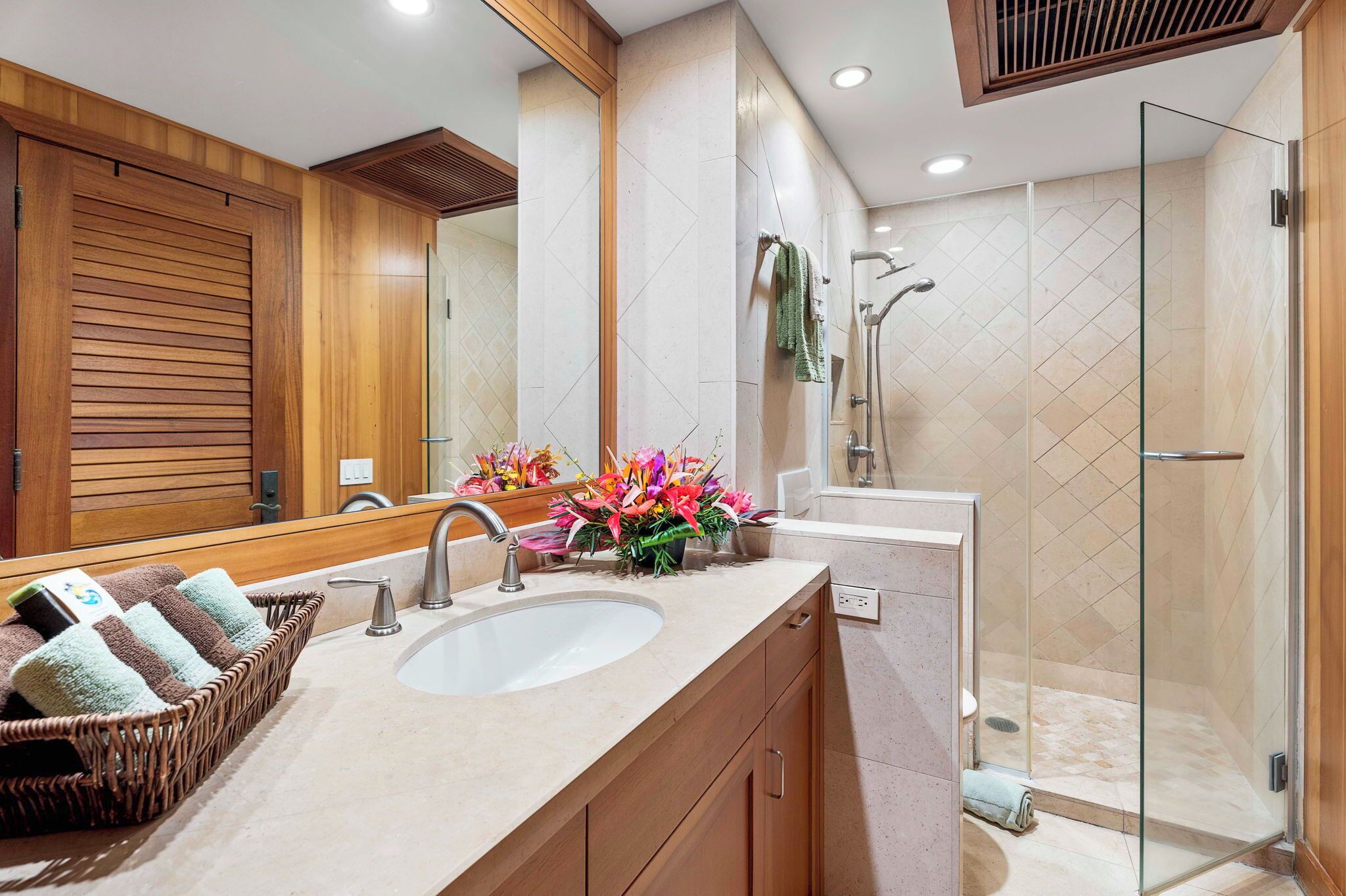 Un baño moderno con un espejo grande, muebles de madera, un lavamanos y una cabina de ducha con paredes de vidrio.
