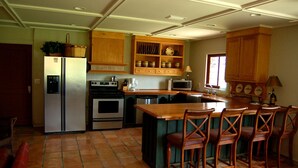 Una cocina equipada con refrigerador, estufa, microondas, gabinetes de madera y una barra con sillas.
