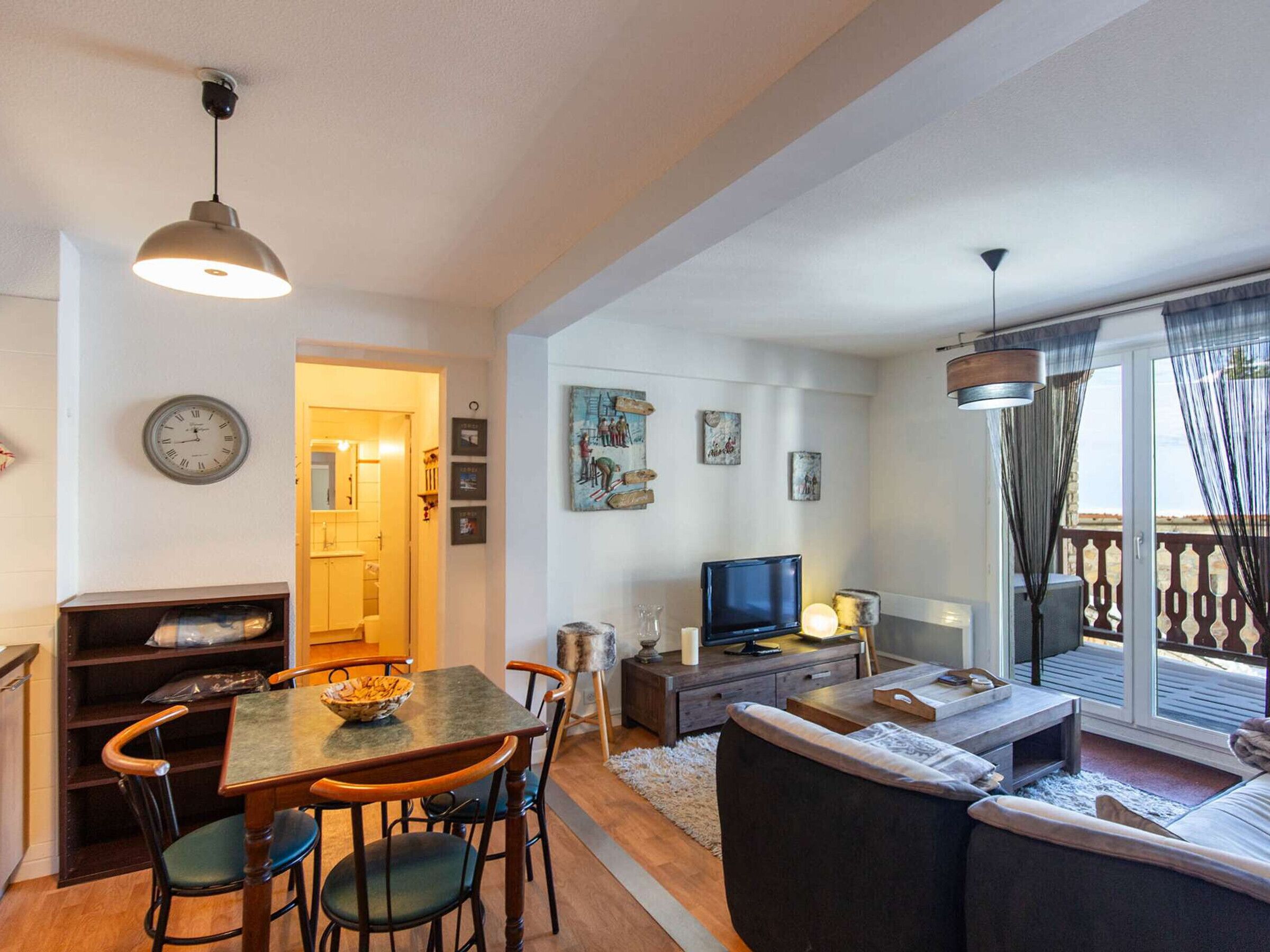 Een woonkamer met een bank, televisie en een eethoek met stoelen en een tafel.
