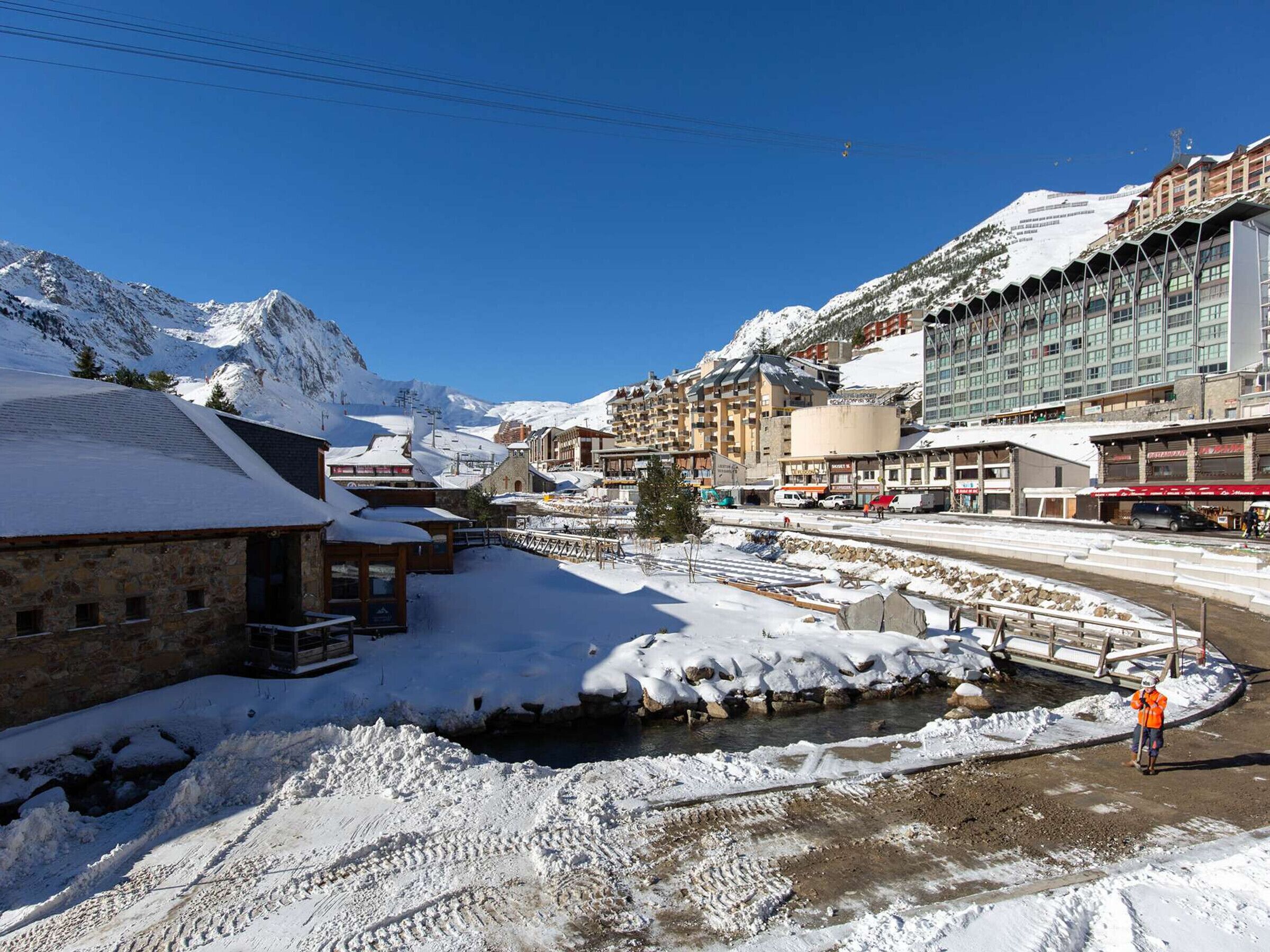 Un pueblo cubierto de nieve con un río, edificios y montañas al fondo.