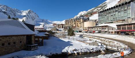 Un pueblo cubierto de nieve con un río, edificios y montañas al fondo.