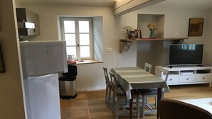 A compact living space with a dining table, chairs, a refrigerator, a coffee maker, a television, and a small window. - Apartment in Basque house (Sare)