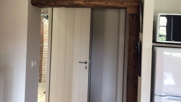 A narrow hallway with a wooden beam ceiling, a white door, and a refrigerator on the right. - Apartment in Basque house (Sare)