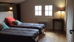 A bedroom with two beds, a radiator, a window, and a bedside table with a lamp. - Apartment in Basque house (Sare)