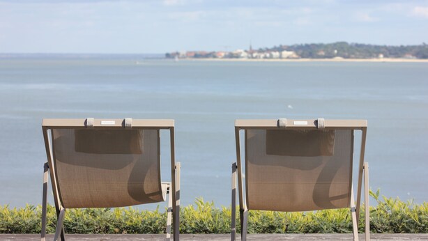 Deux chaises de plage sont placées face à une mer calme, avec une côte visible au loin.