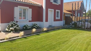 Une maison rouge avec des volets blancs, un petit balcon et une pelouse bien entretenue.