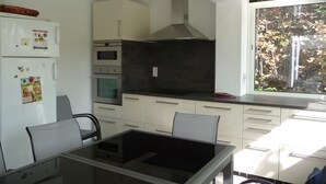 A modern kitchen with a glass dining table, white cabinets, and a large window.