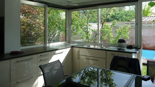 A modern kitchen with a large window, a sink, and a dining area with a glass table.