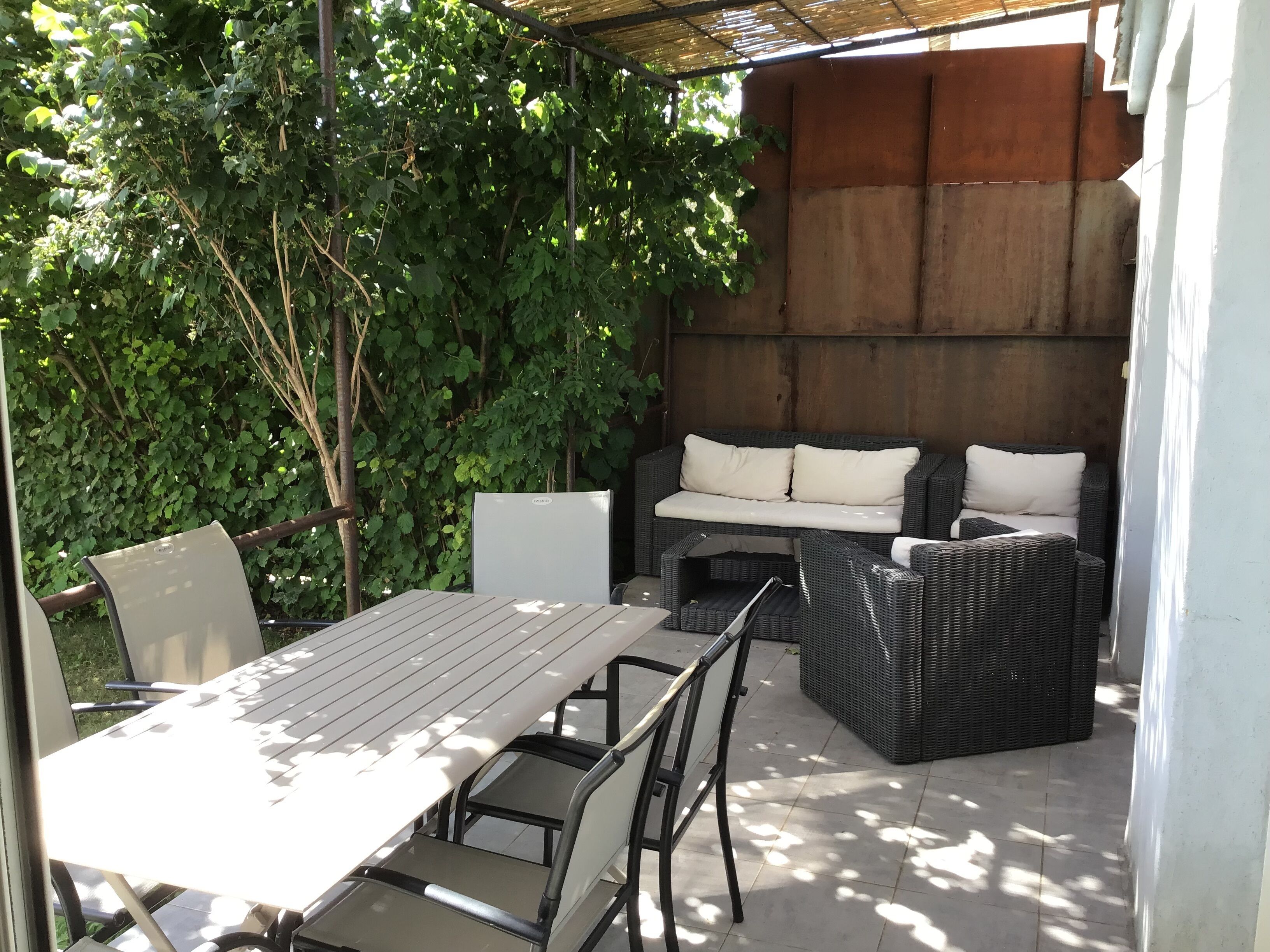 An outdoor patio with a table and chairs, a wicker sofa, and a pergola.