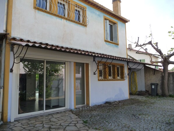A two-story building with large glass doors and windows, a tiled roof, and a stone-paved courtyard.
