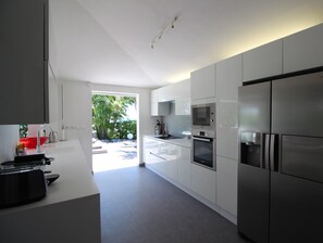 Una cocina moderna con armarios blancos, electrodomésticos de acero inoxidable y vistas a zonas verdes.