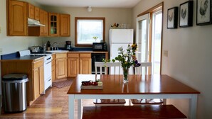 Une cuisine avec des meubles de rangement en bois, un réfrigérateur blanc et une table à manger agrémentée d’un vase de fleurs.