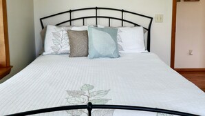 Un lit avec un cadre en métal et une literie ornée de motifs de feuilles, un tableau représentant un animal blanc accroché au mur, et une porte décorée d’une image de fruits.