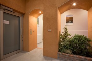 A hallway with a glass door, a brick planter with greenery, and a framed picture on the wall.