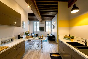 A modern kitchen with wooden beams, a dining area with clear chairs, and a black sink.