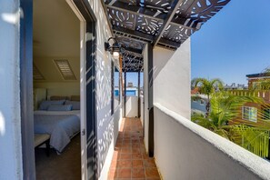 A narrow balcony with a bed, a patterned wall, and a view of the sea.