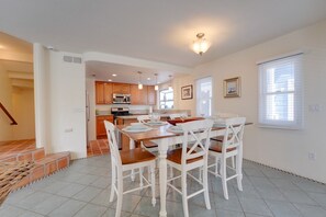 Una cocina moderna con armarios de madera, una mesa de comedor con sillas blancas y una escalera que lleva a otro nivel.