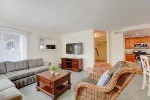 A living room with a sofa, a coffee table, a TV, and a wicker chair.
