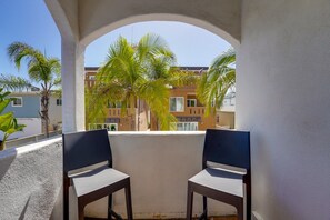 A balcony with two chairs, a view of palm trees, and buildings in the background.