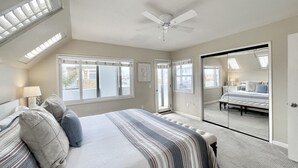 Un dormitorio con una cama grande, ventilador de techo, tragaluces, puerta corrediza al balcón y vistas al exterior.