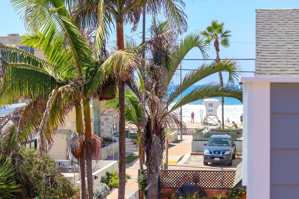 A view of a beach with palm trees, a lifeguard tower, and a parked car.
