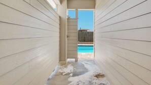 A narrow corridor with light-colored wooden walls leading to a pool area. - 🌊 Sealation! – Luxe 8BR w/ Pool | Game Room | Rooftop Deck | Elevator 🌊 (Pensacola Beach)