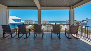 A covered outdoor area with six rocking chairs facing a beach view. - 🌊 Sealation! – Luxe 8BR w/ Pool | Game Room | Rooftop Deck | Elevator 🌊 (Pensacola Beach)