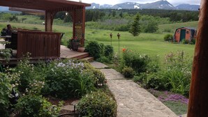 Un jardin agrémenté d’une pergola en bois, d’un chemin de pierre et offrant une vue sur les montagnes en arrière-plan.