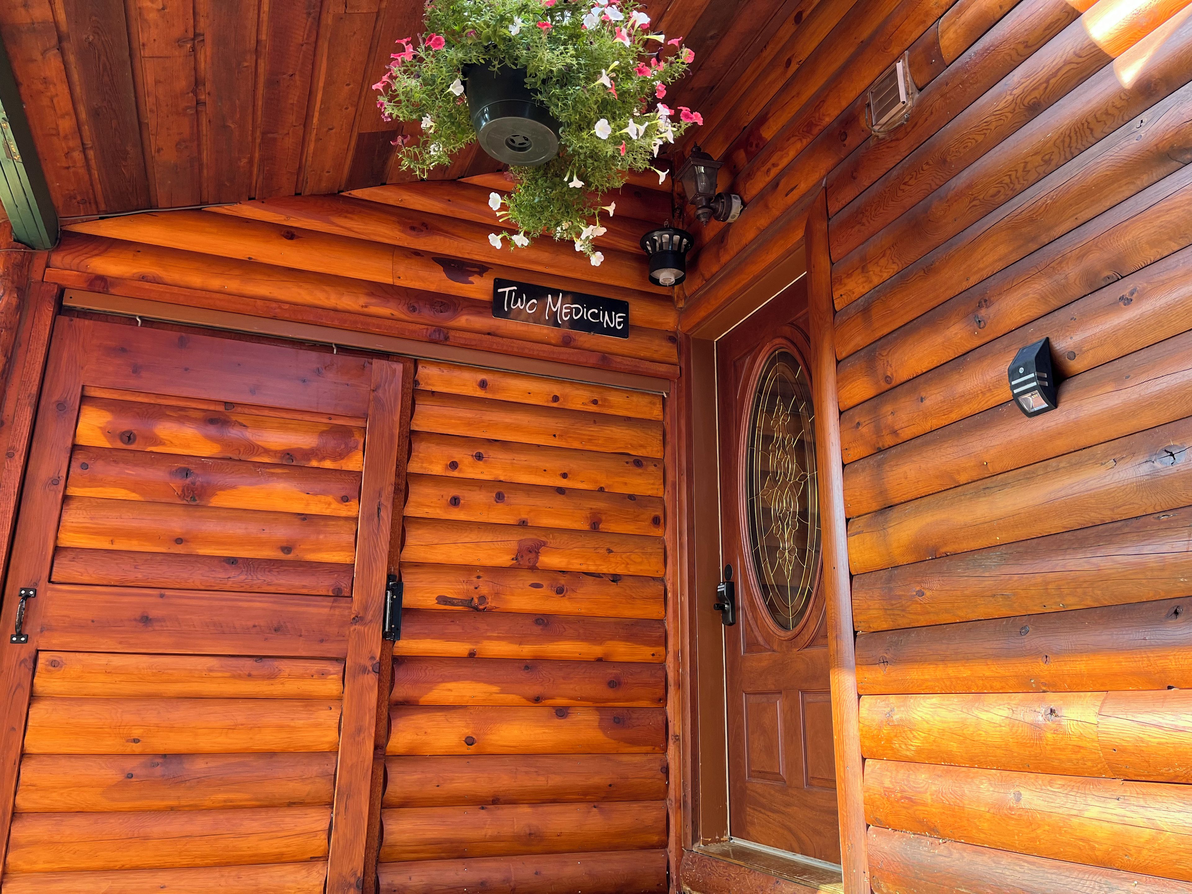 A wooden door with a sign above it, a hanging flower pot, and a wall-mounted light fixture.