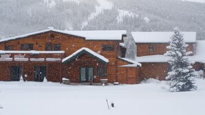 Une cabane en bois, dont le toit est recouvert de neige, avec un arbre également couvert de neige devant.