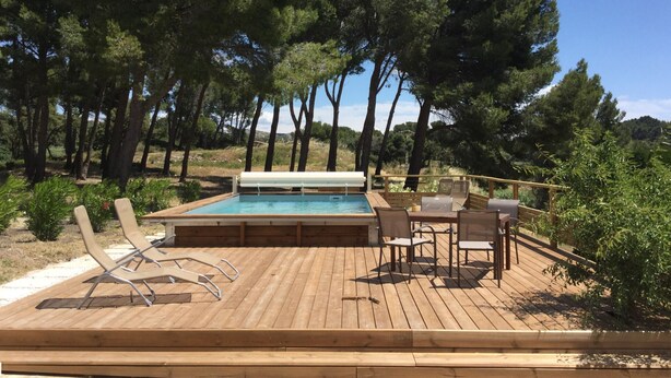 Terraza de madera con piscina, sillas de descanso y una mesa.
