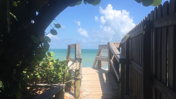 Un sentier en bois mène à une plage, avec une clôture en bois d’un côté et un banc de l’autre.