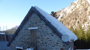 Un bâtiment en pierre avec un toit en pente recouvert de neige, une porte en bois et une enseigne indiquant « VENTE DE FROMAGE ».