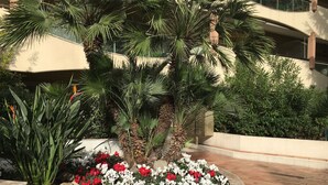 Un espace paysager agrémenté d’un palmier, de fleurs rouges et blanches, et de divers arbustes.