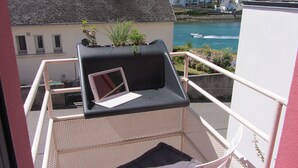 Varanda com um laptop em um assento acolchoado, com vista para um corpo de água e edifícios.