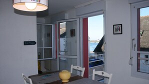 Um quarto com uma mesa de jantar, cadeiras, um vaso amarelo, uma janela com vista para o mar e uma placa com o texto "La Plage".