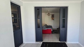 Un couloir avec un canapé rouge, un banc noir et une porte dotée de volets sombres.