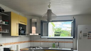 Une cuisine de taille réduite avec des placards jaunes, une cuisinière à gaz, un four à micro-ondes, un évier, un lave-linge et une fenêtre avec des stores.