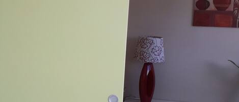 Une pièce avec une porte fermée, un vase rouge posé sur une table blanche et un tableau accroché au mur.