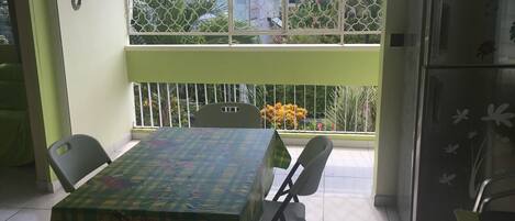 A dining area with a table and chairs, a refrigerator, and a view of the outside through a window with a metal fence.