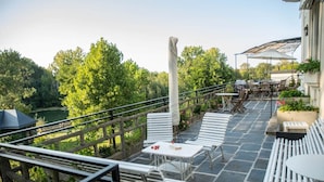 Eine Terrasse mit weißen Metallmöbeln, Steinboden und Blick auf Grünflächen.