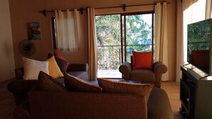 A living room with two sofas, a TV, and a balcony with a view of palm trees and buildings. - 1 Bedroom Apartment in Flat Area Near the Beach and Zocalo  (Bucerías)