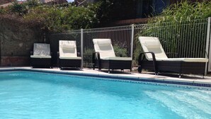 A swimming pool with clear blue water, surrounded by a metal fence. There are three lounge chairs with white cushions and dark wicker frames. - Private Courtyard and Pool, close to Carcassonne and Mediterranean Beaches (Argeliers)