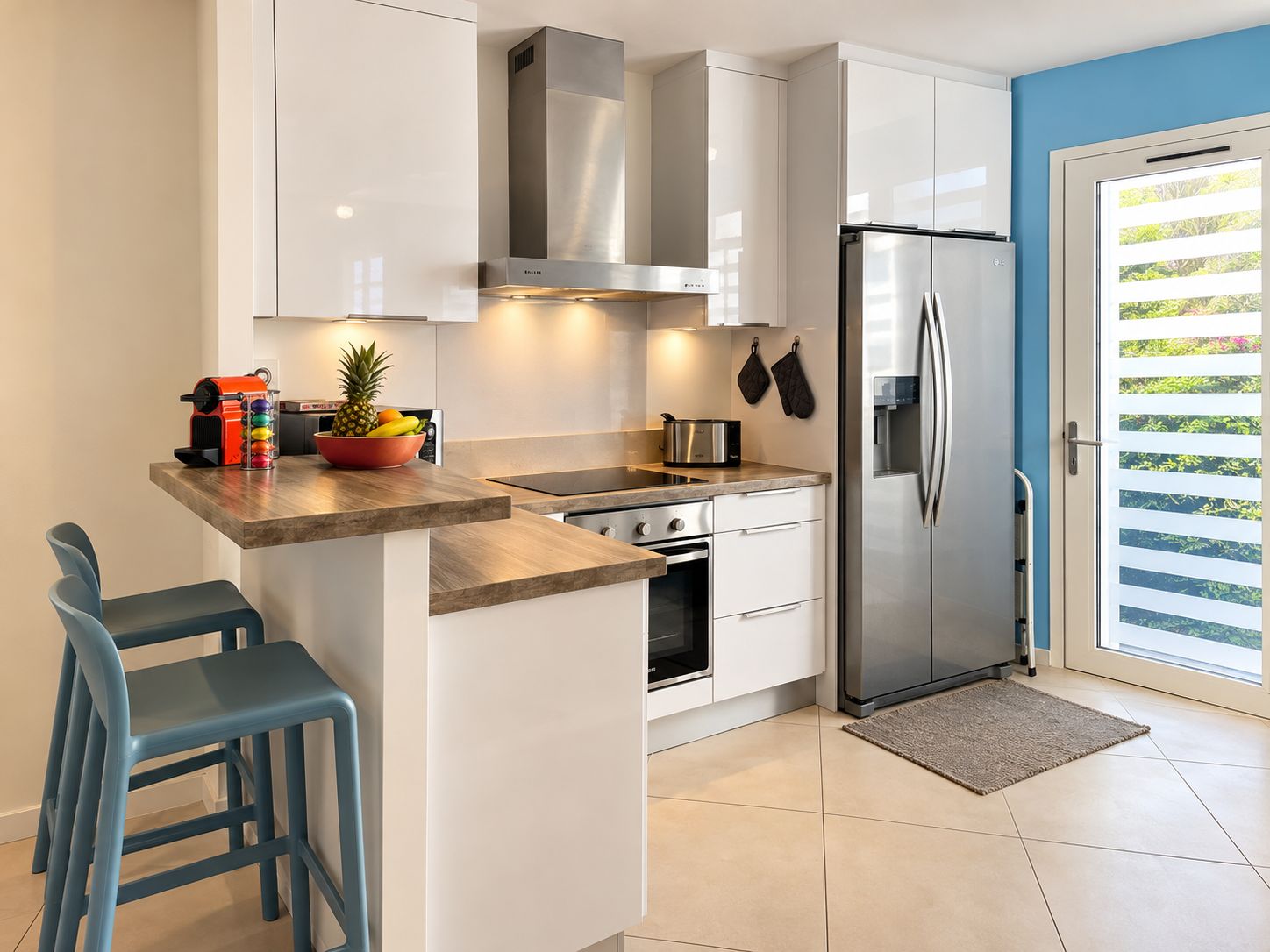 A modern kitchen with a built-in oven, a stainless steel refrigerator, and a window with blinds.