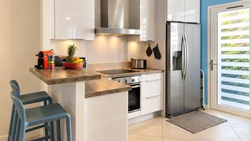 A modern kitchen with a built-in oven, a stainless steel refrigerator, and a window with blinds.
