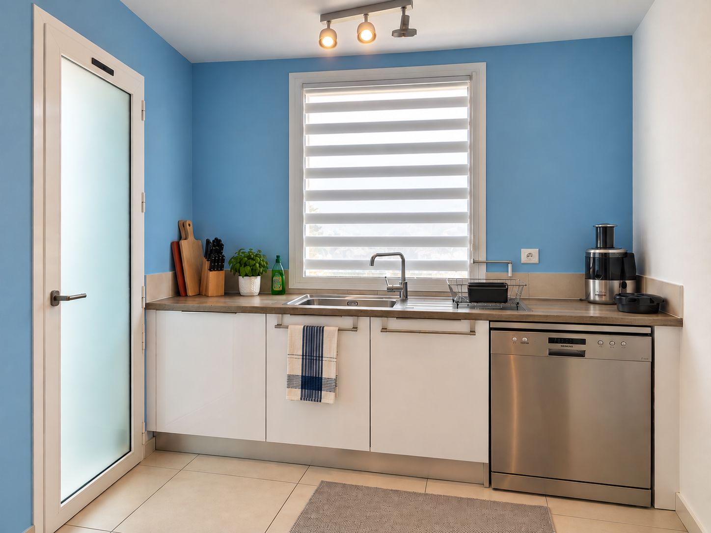 Een moderne keuken met een vaatwasser, een koffiezetapparaat en een raam met zonwering.