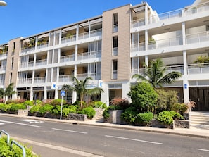 A multi-story hotel with balconies, a street in front, and greenery.