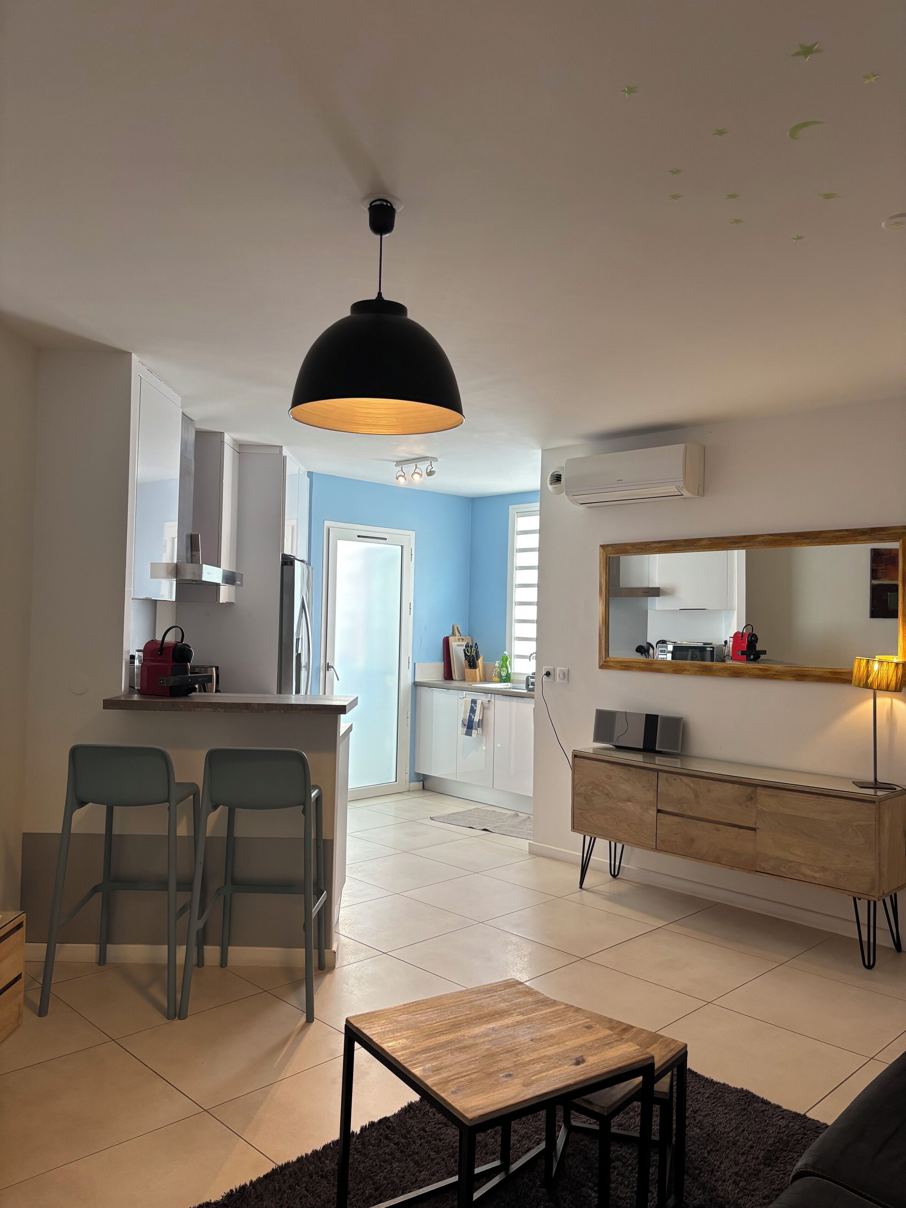 A modern kitchen with white cabinets, a black pendant light, and a small island with a kettle.