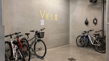 Pyöräparkki, jonka seinässä on sana »VELO», pyöräteline ja seinälle ripustettu kypärä.